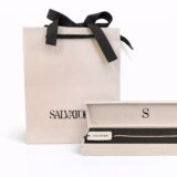 Bolsa de regalo de la marca Salvatore junto a una caja abierta que muestra una pulsera dorada, destacando la elegancia y el diseño de la joyería.