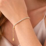 Pulsera de oro con cristales brillantes, lucida en la muñeca de una mujer con blusa satinada. Ideal para ocasiones especiales y complementos de moda.