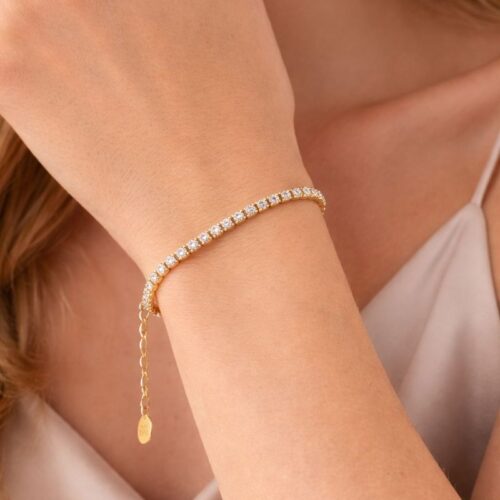 Pulsera de oro con cristales brillantes, lucida en la muñeca de una mujer con blusa satinada. Ideal para ocasiones especiales y complementos de moda.